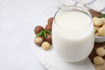 Glass of macadamia milk and nuts on white tiled table, closeup. Space for text