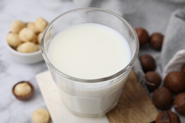Glass of macadamia milk and nuts on white marble table, closeup
