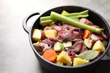 Cooking stew. Uncooked meat and vegetables in pot on light grey table, closeup