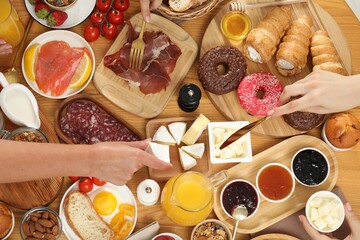 Women eating different food during brunch at wooden table, top view