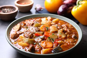Delicious stew with vegetables in bowl and ingredients on grey table, closeup