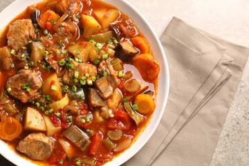 Delicious stew with vegetables in bowl on light grey table, top view