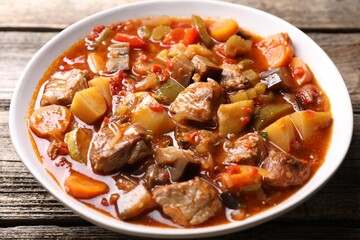 Delicious stew with vegetables in bowl on wooden table, closeup