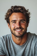 Obraz premium A young man smiles brightly, showcasing his cheerful demeanor while dressed casually in gray