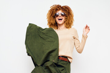 Stylish woman with curly hair wearing sunglasses, posing playfully with a green cloth against a...