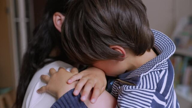 Young boy upset and crying, being comforted by his mother while they embrace. The child is sad and emotional, seeking comfort and care from the supportive parent