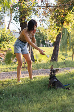 Smiling young woman walks and plays with a small dog in public park,