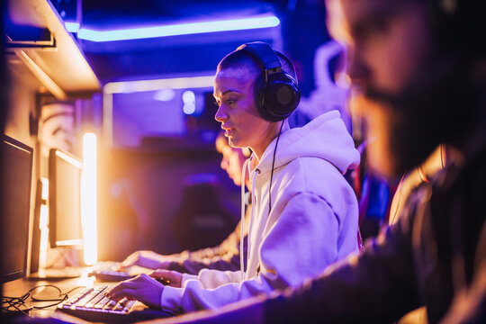 Focused gamer girl with headset sitting in cybercafe, playing mmo game