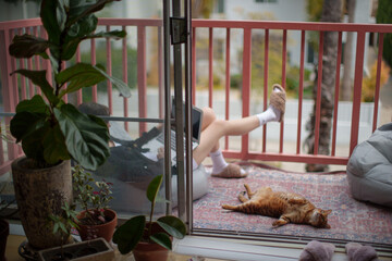 A cat lounges on its back on a patterned rug on a balcony, while in the background a woman is seen...