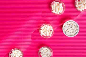 Dietary supplements pills in white colour from above on a pink background.
