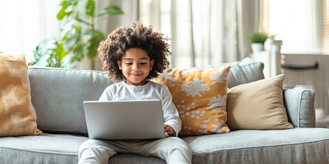 Naklejka premium friendly young child using laptop computer, sitting on living room couch