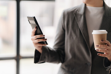 Businesswoman on the Go: A close-up shot of a stylish businesswoman holding a smartphone and a cup of coffee, highlighting her busy and professional lifestyle. The image captures the essence of modern