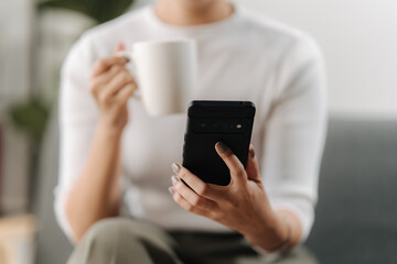 Morning Scroll: Woman enjoys her morning coffee while catching up on her smartphone, embracing the comfort of home and digital connection. 