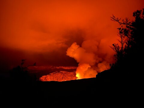 A cloud of smoke, bathed in an orange glow, rises above a volcanic eruption at Kīlauea volcano.