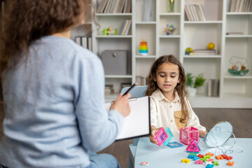 Naklejka premium Cute little girl sitting at the table and having a training session with speech therapist