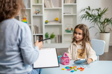 Cute little girl sitting at the table and having a training session with speech therapist