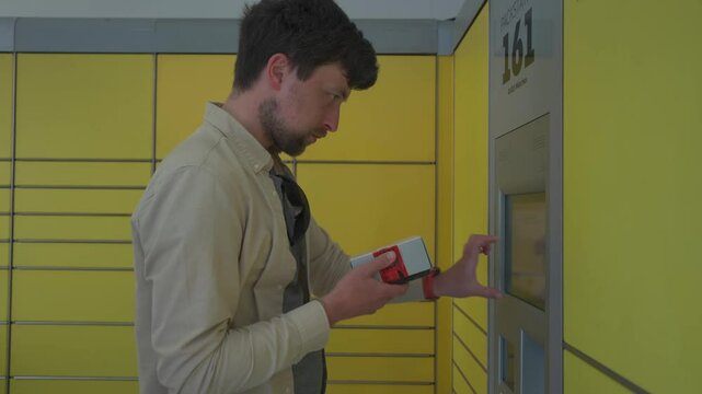Male customer using self-service automated delivery terminal to send package or storage locker to drop off parcel. Postal automatic package pickup point man at operating screen holding phone and box. 
