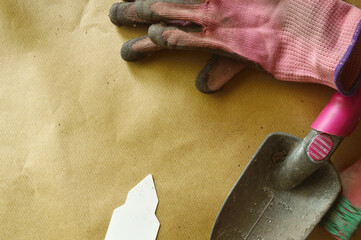 gardening themed, planting table, flat lay, white tag, pink working gloves, pink trovel, beige wrapping paper covered table, top view, copy space,