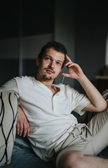 Obraz premium A young man in a relaxed pose on a bed, wearing a casual white shirt. He appears thoughtful and at ease in an intimate indoor setting.