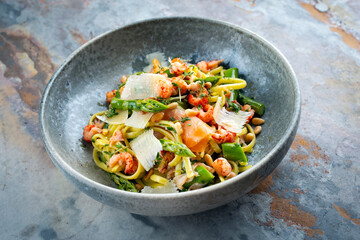 Traditional Italian Pasta with green Green asparagus, prawns and smoked salmon slices served with pine nuts and parmesan cheese slices as close-up in a Nordic design bowl