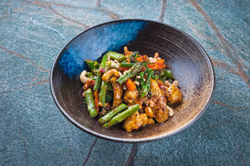 Traditional spicy chicken fillet nuggets with green asparagus, cashew nuts and broccoli in sweet sour sauce served as close-up in a design bowl with text space