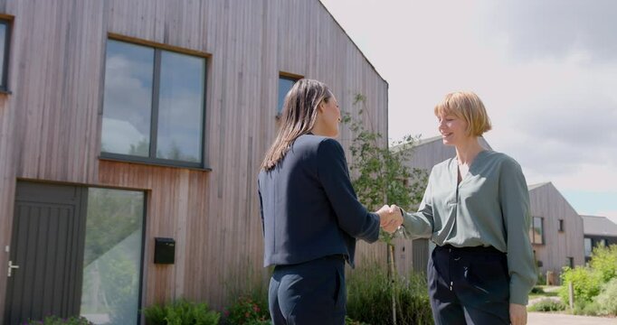 Real estate agent Shaking hands with Mature Woman Outside Property for Sale