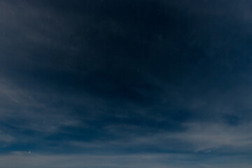 Obraz premium A serene, expansive lake reflects the soft glow of a starry night sky. Wispy clouds stretch across the horizon, adding to the calm, tranquil atmosphere. The distant shoreline is faintly visible