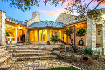 Stunning stone house with large windows and landscaped garden at sunset in a serene setting