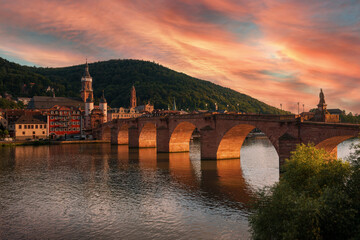 The Old Bridge in Heidelberg, Germany, with dramatic orange light at sunset. Colorful clouds in the...