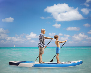 Boy and elderly man paddling a SUP board together in the sea