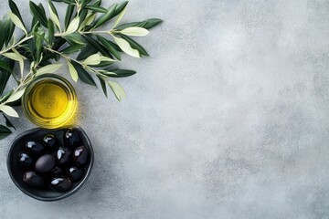 Top view of a small bowl with black olives and extra virgin olive oil surrounded by olive tree branches on a gray concrete surface with room for text