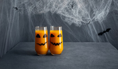 Halloween drink on blue background. Pumpkin or carrot juice in glasses with jack o lantern face....