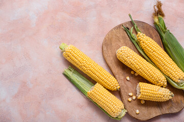 Wooden board with fresh corn cobs on beige table