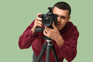 Male photographer with modern camera on tripod against green background