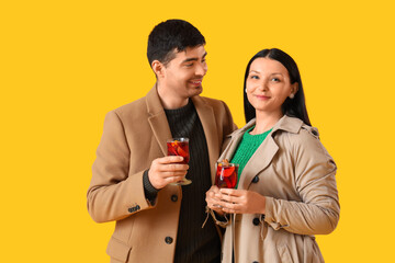 Young couple with glasses of mulled wine on yellow background