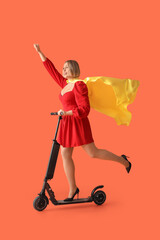 Beautiful mature happy woman with kick scooter and superhero cape on orange background