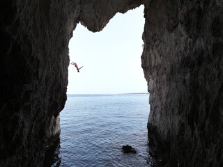 Man Backflipping off a cliff into water, shot from inside a cave looking out to the ocean