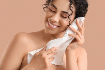 Young African-American woman removing makeup with towel on beige background, closeup