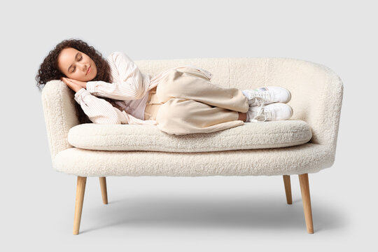 Beautiful young happy African-American woman sleeping on sofa against grey background - Powered by Adobe