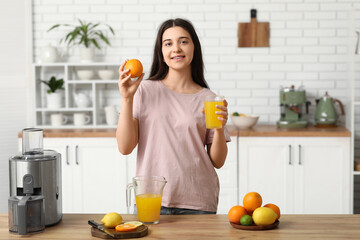 Obraz premium Beautiful young woman with glass of fresh orange juice in kitchen
