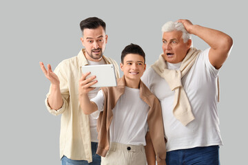 Teenage boy with his dad and grandfather using tablet computer on light background