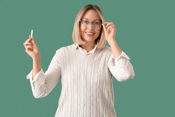 Mature female math teacher holding chalk on green background