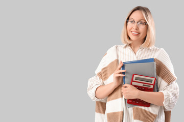 Mature female math teacher with calculator and notebooks on grey background