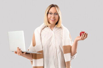 Mature female math teacher with laptop and apple on grey background