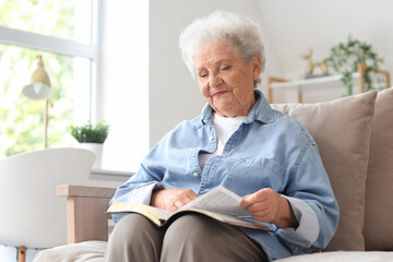 Senior woman on sofa reading Bible at home