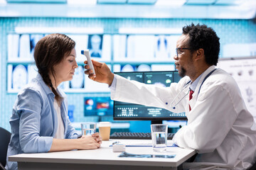 Fototapeta premium General practitioner using a thermometer to measure fever on a female patient, doing a check up visit examination with modern medical tools. Doctor specialist checking temperature on a woman.