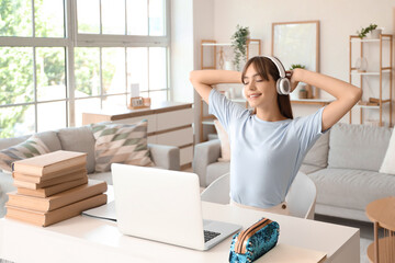 Happy female student in headphones with books and laptop studying at home