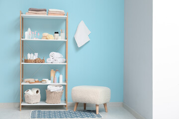 Modern shelving unit with bath accessories and pouf near blue wall in room