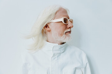 elderly man with long white hair and glasses, wearing a white jacket against a light background,...
