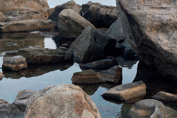 Tranquil ocean scene with clear water, rocks, and boulders scattered along the shore